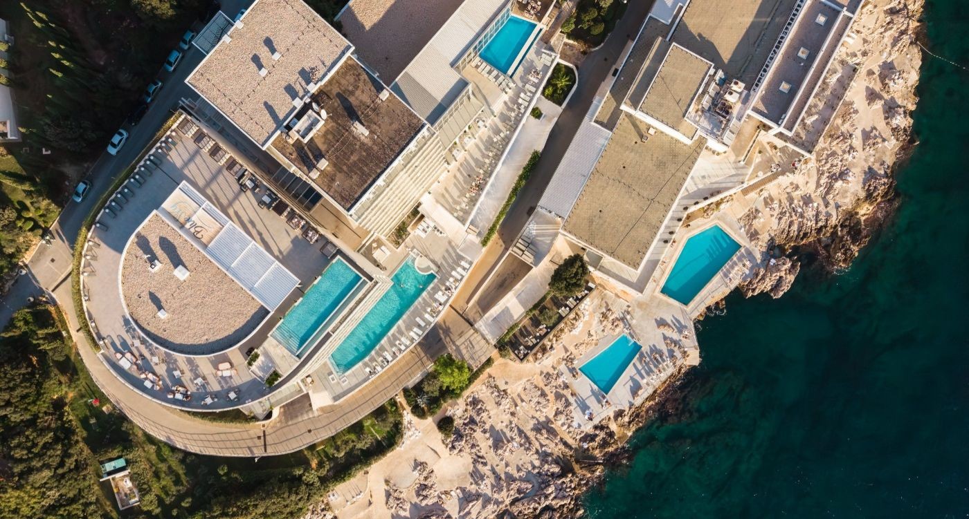 Aerial view of Royal Blue and Royal Neptun hotels in Dubrovnik, showing outdoor swimming pools, the beach and the Adriatic Sea.